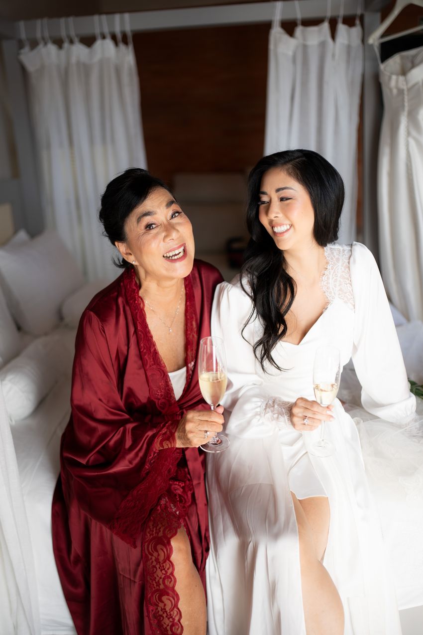 Noiva e sua mãe de robes brindando com espumante no quarto