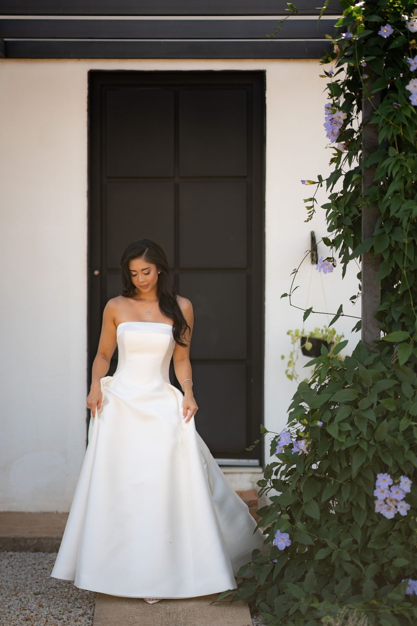 Noiva segurando a saia do vestido ao lado de flores lilás