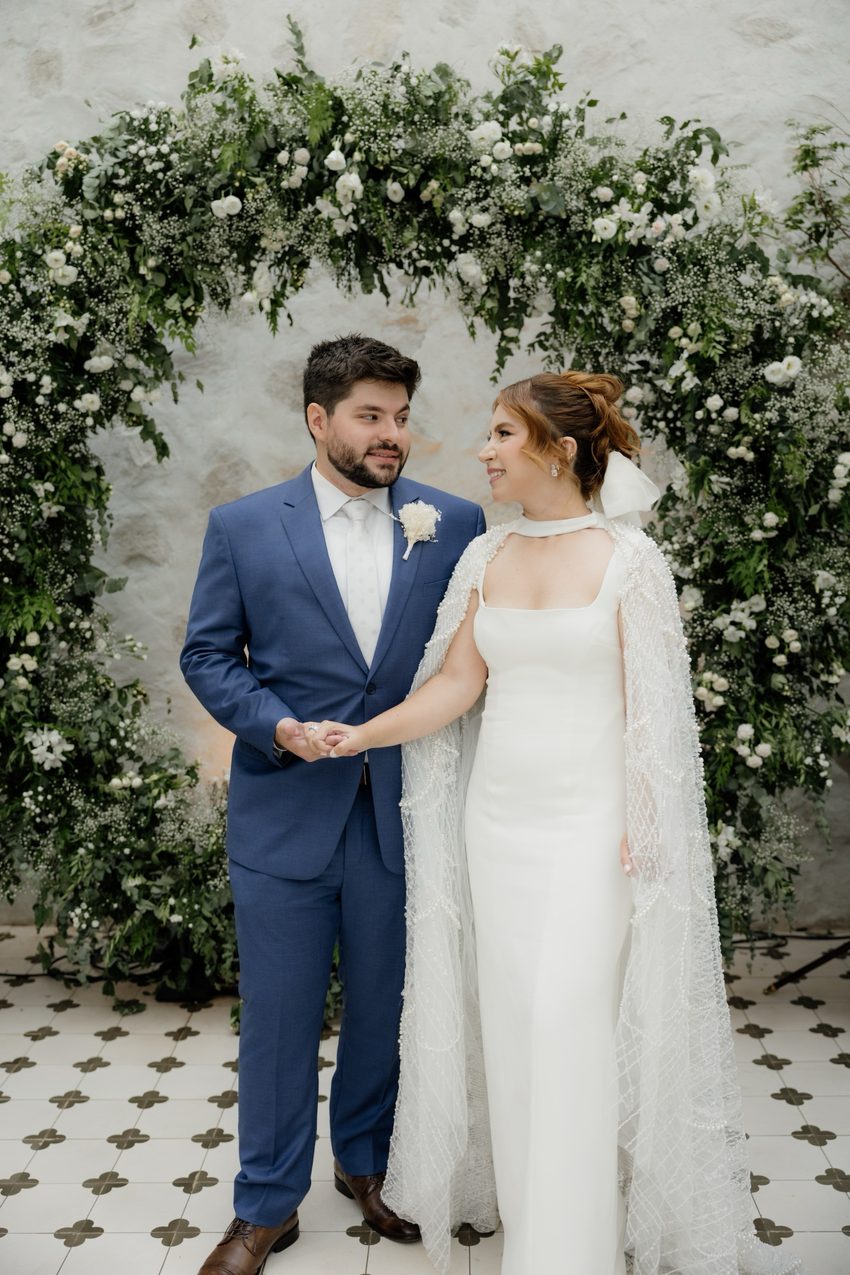 Casal no arco floral, olhando um para o outro